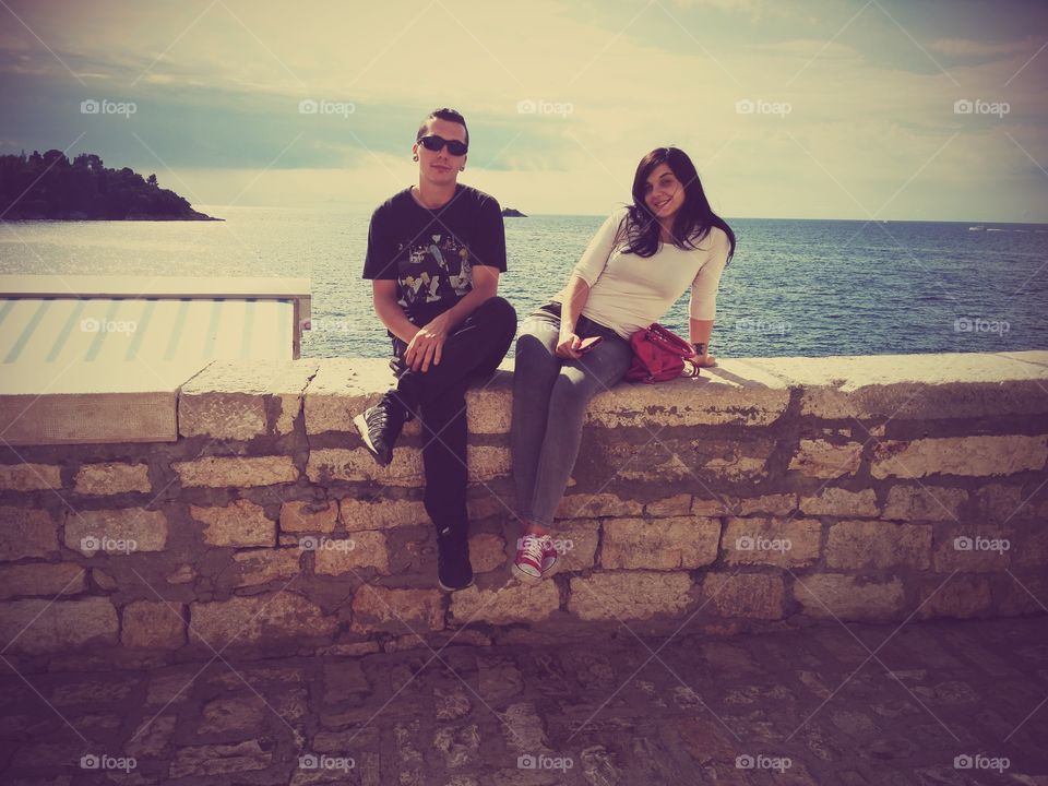 Happy couple sitting on retaining wall in front of sea