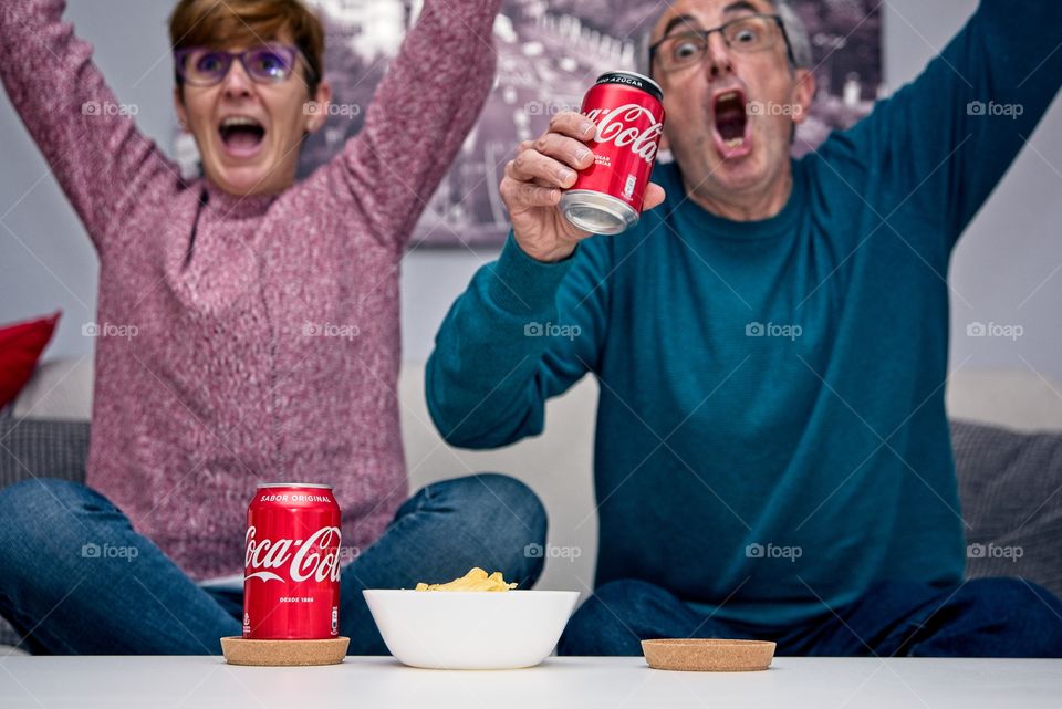 Couple eating a snack with Coca Cola while watching football