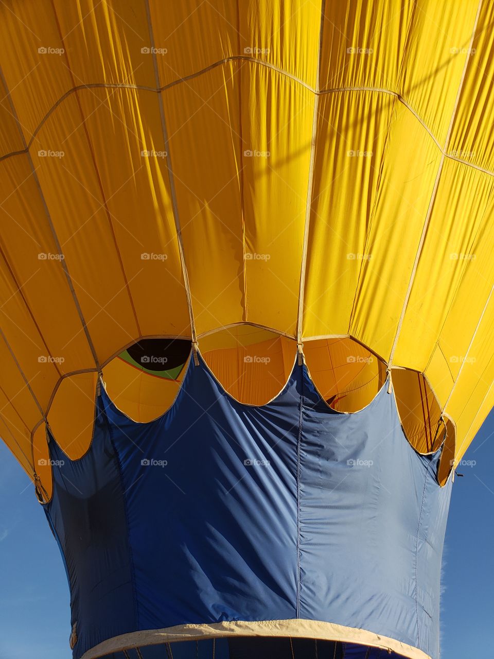 Lower part of a hot air balloon as it gets inflated. Bright yellow against blue sky background.