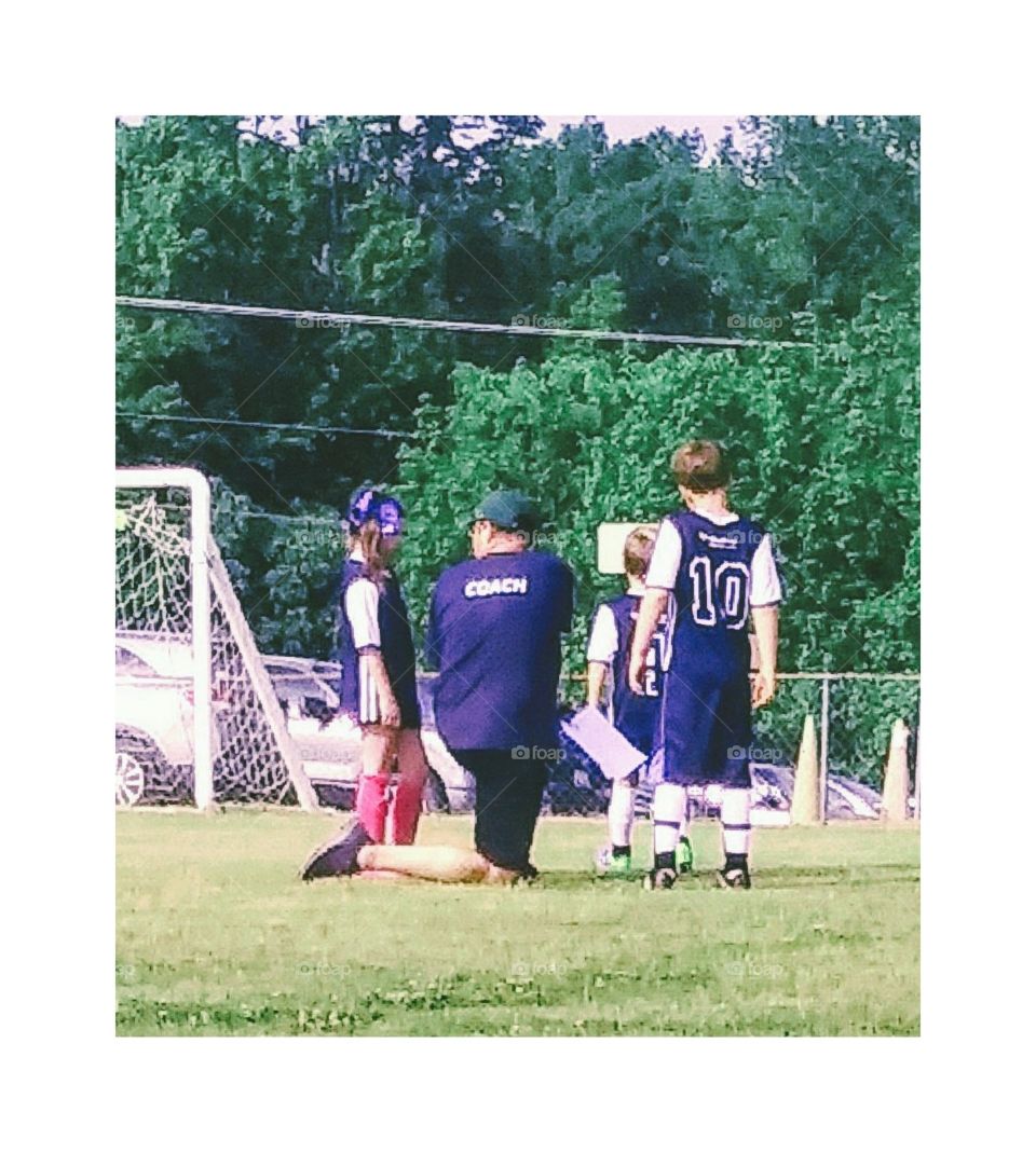 Young girl and young boy getting tips from their coach in a huddle during game