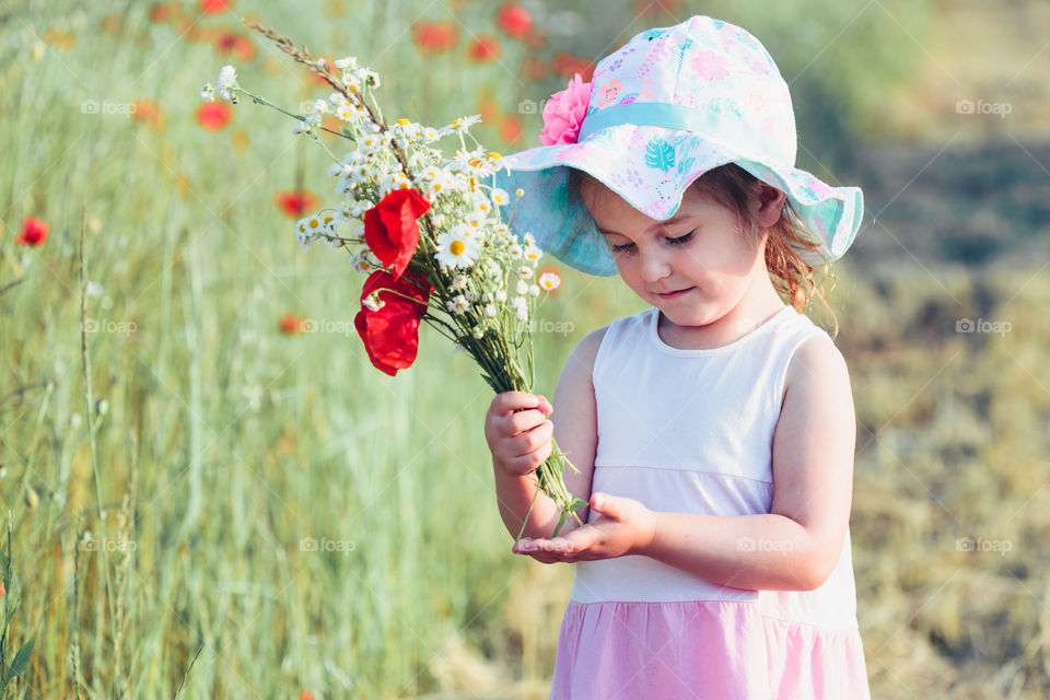 Lovely little girl in the field of wild flowers. Cute girl picking the spring flowers for her mom for Mother's Day in the meadow. Girl holding bouquet of flowers. Spending time close to nature