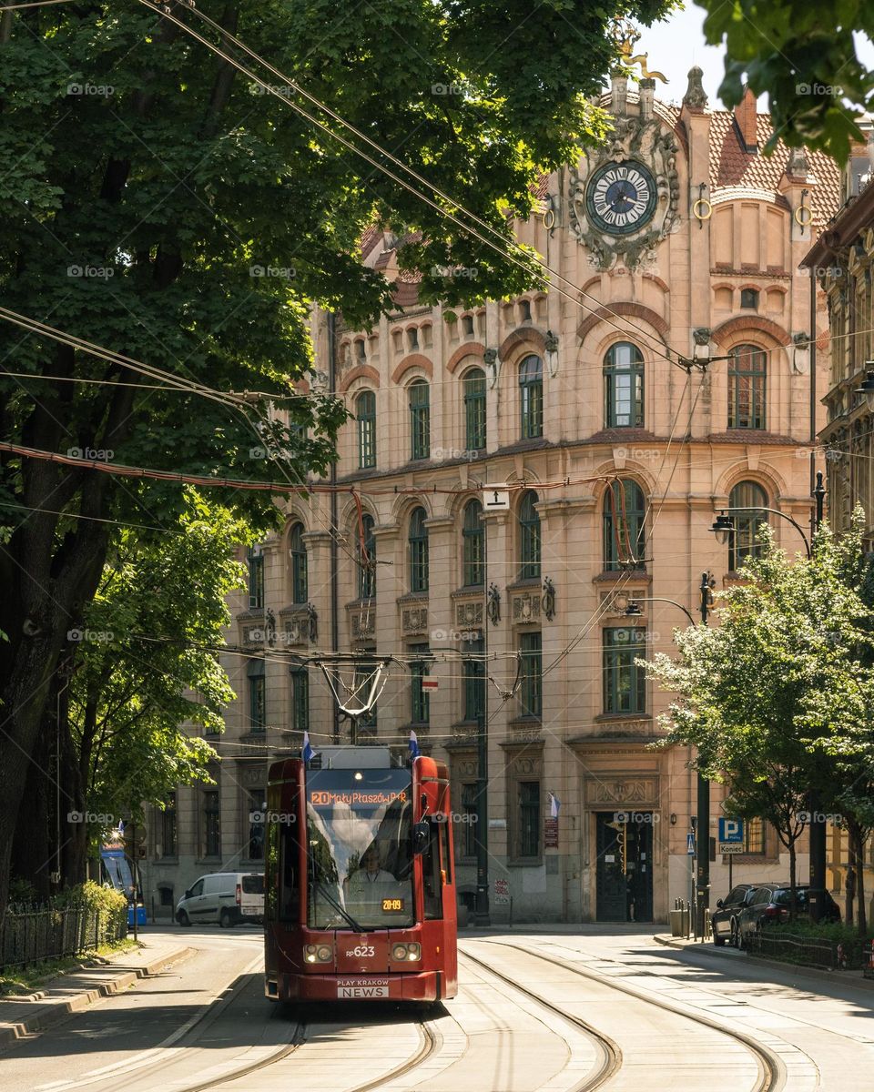 the tram goes along the street along the Planty park in Krakow in the background a beautiful school building