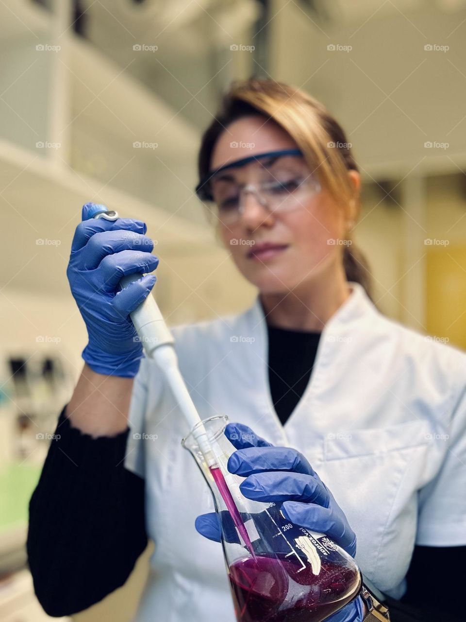 Woman in laboratory pipetting with automatic pipette from conical flask