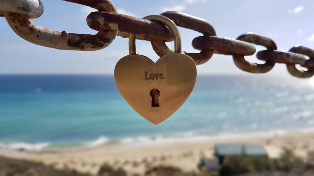 Love, heart shaped padlock hanging on metal chain, by the ocean 