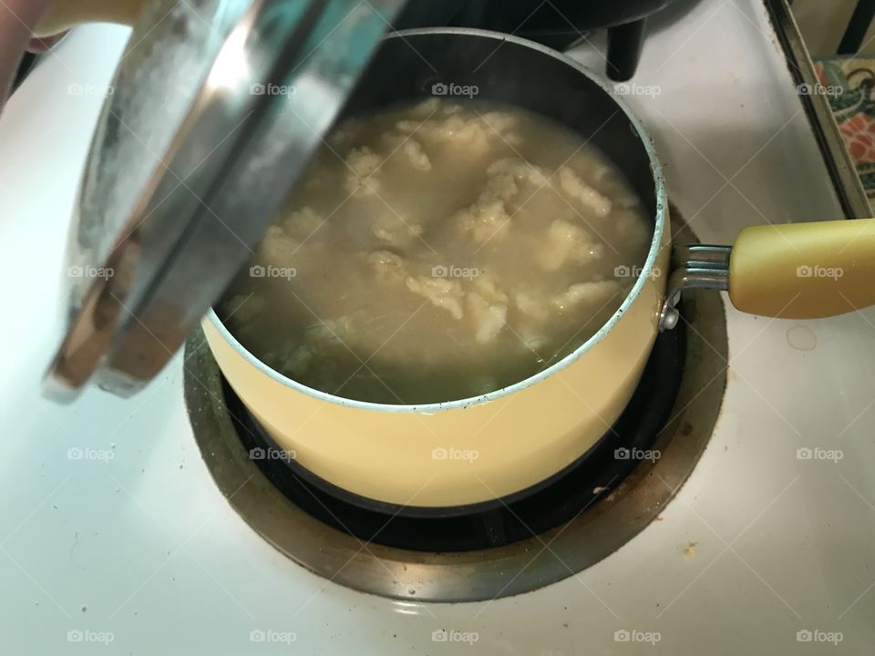 Homemade noodle dumplings rivets in chicken broth; cooking on the stove top in pot  
