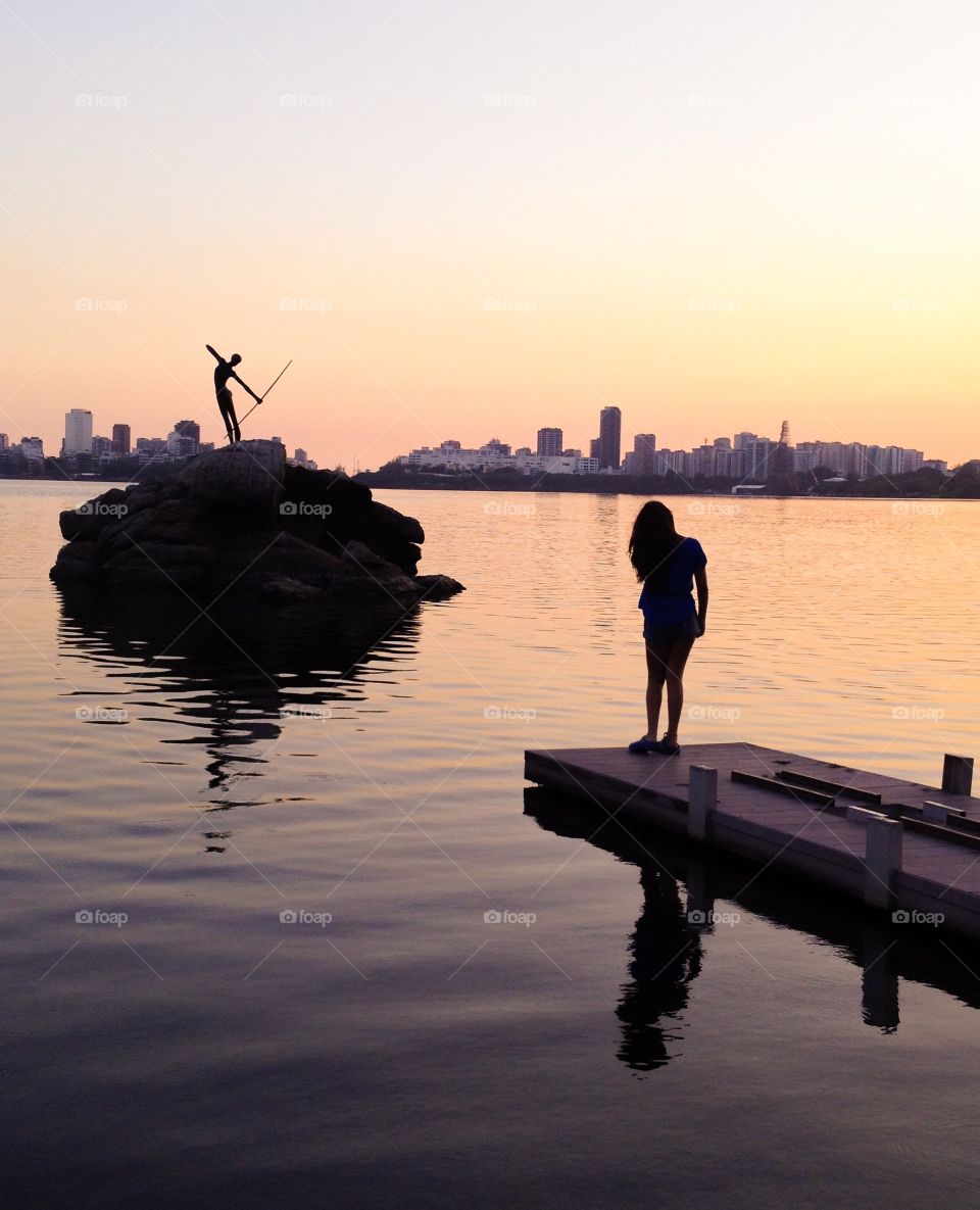 A girl watching the sunset at the edge of a lake