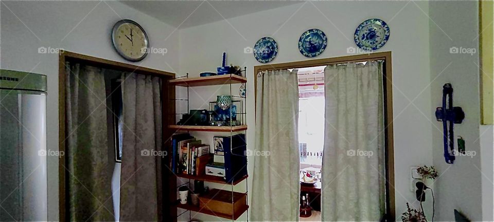 This is the kitchen of the house in „Bavaria“, Germany taking us back to where we started: the doors to the front entrance and the living room with thermo curtains, the clock, decorative plates and the shelves. 2023. Hypnotic Productions