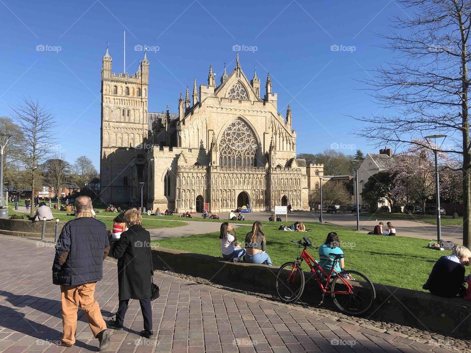 Exeter Cathedral in exceptional sunny spring like weather, with plenty of folk taking advantage of the sunshine, weather by foot or bike.
