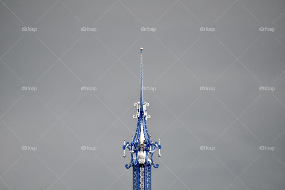 The top of An ornate blue and silver tower with a steeple reaching to the grey cloudy sky