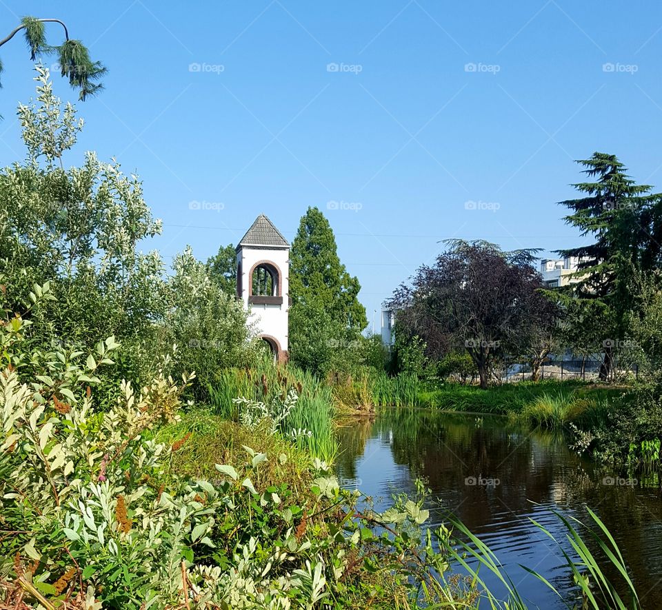 A forgotten clock tower bridge across a pond.