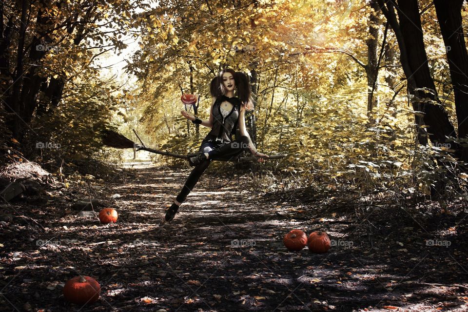 Woman dressed in witch costume sitting on broom stick