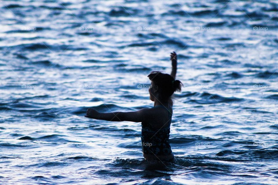 Silhouette of my middle daughter dancing in the inky blue ocean & smiling as she looks towards the light from the setting sun. Her outstretched arms & the profile of her face shows the joy she feels as she embraces the beauty of the moment.