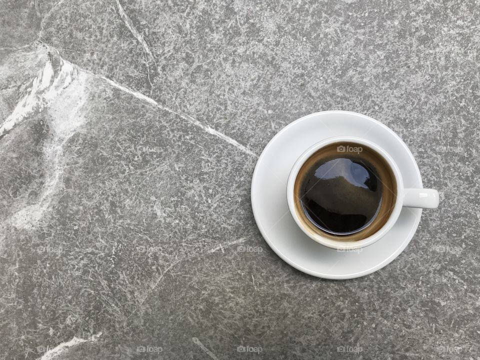 top shot of hot black coffee in white cup with saucer on grey marble table with copy space on left side of frame