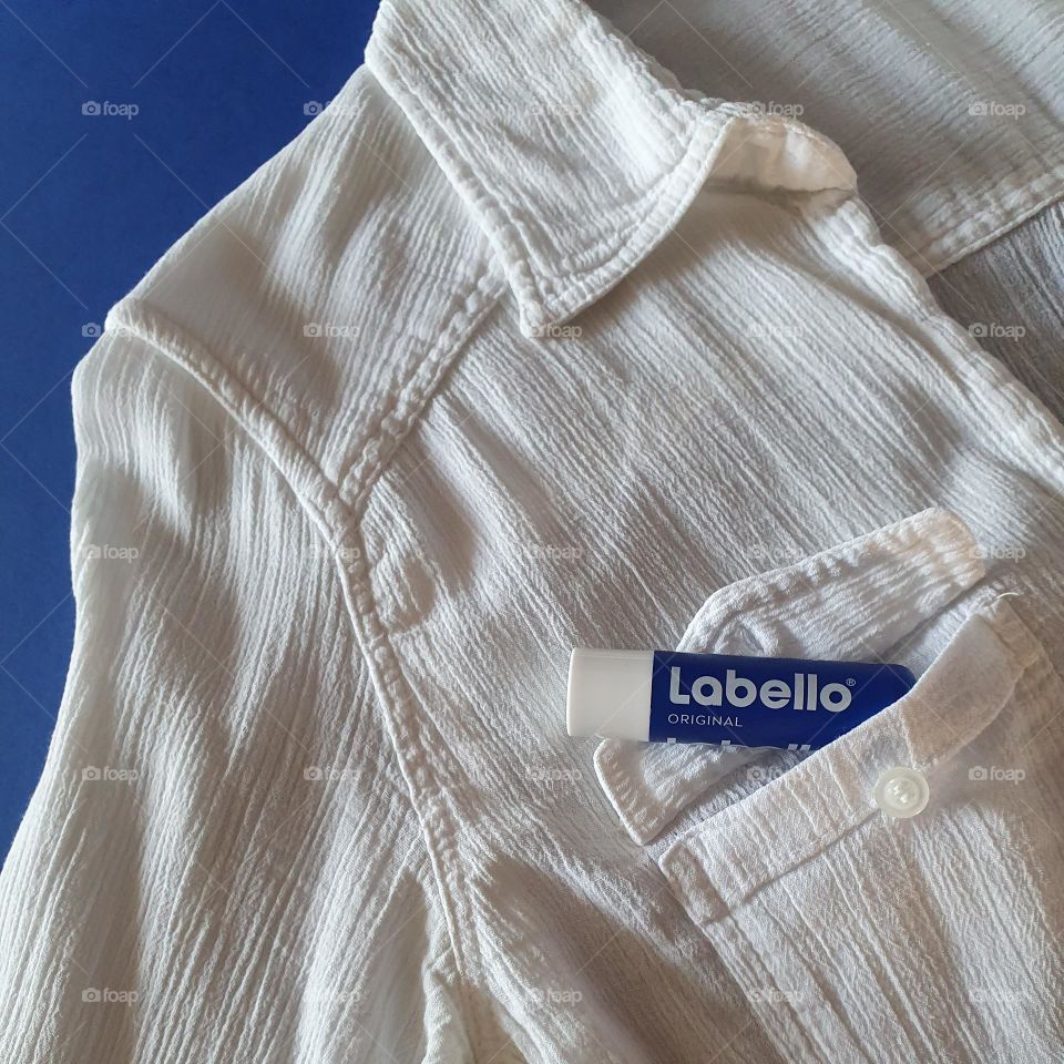 Flatlay on navy blue paper of Labello Original coming out of the pocket of a white shirt