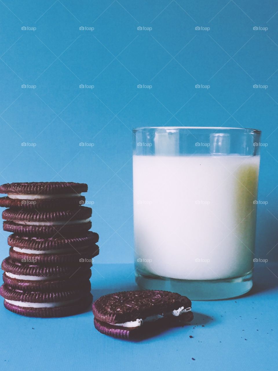 Oreos and Milk. A stack of Oreo cookies with one on its own that been bitten into next to a glass of milk on light blue background 