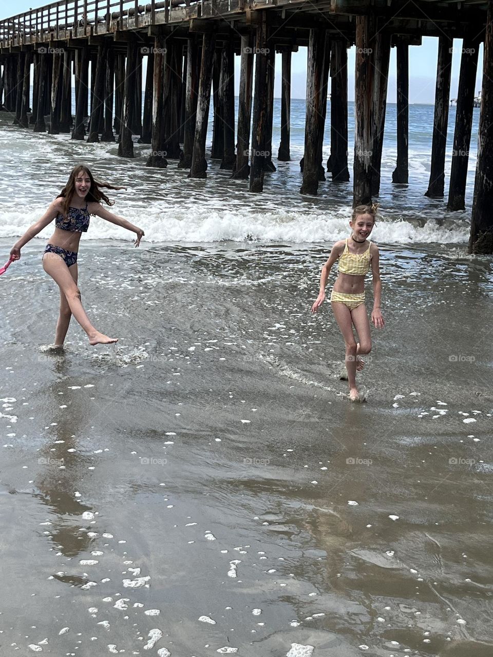 Two girls playing in the water by the pier.