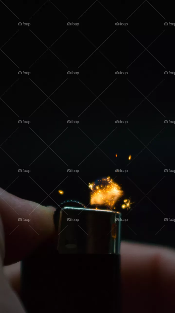 A person has lighters in his hands and he lights it through a flint wheel, the lighter ignites, sparks and fire appear, close-up on a black background.
