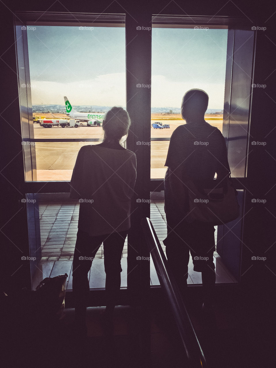 Couple Travelers Looking Outside Of Terminal Window At The Airport
