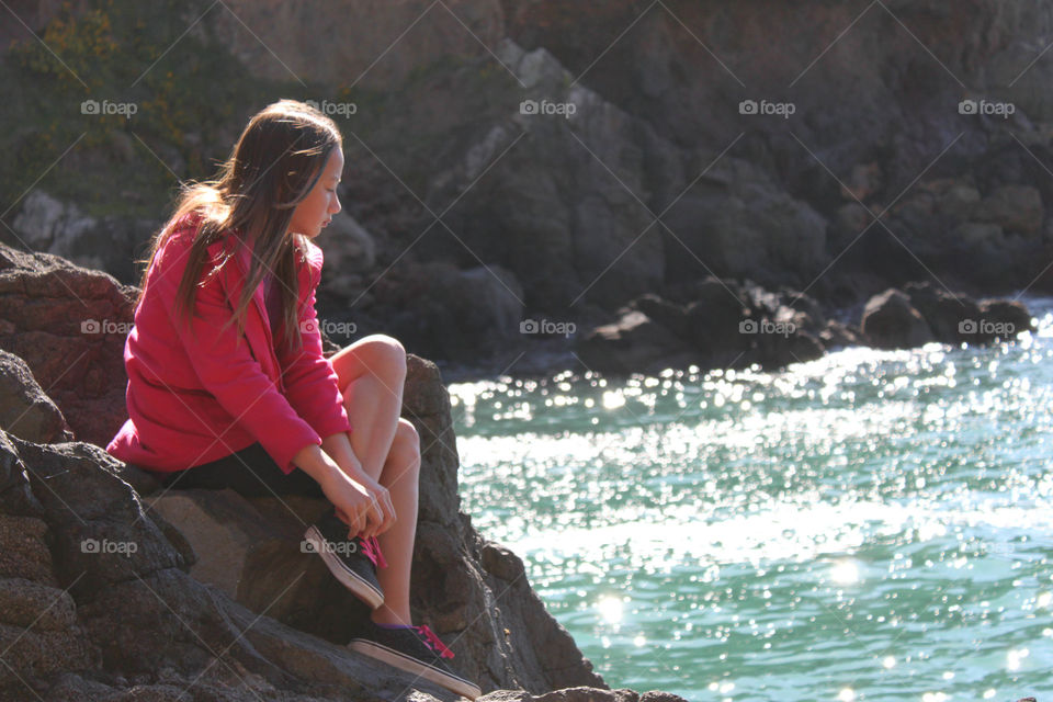 Asian woman sitting on rock at seaside