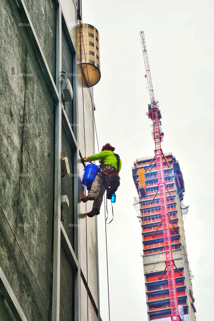 An unrecognizable male construction worker climbs a building with a harness in New York, City