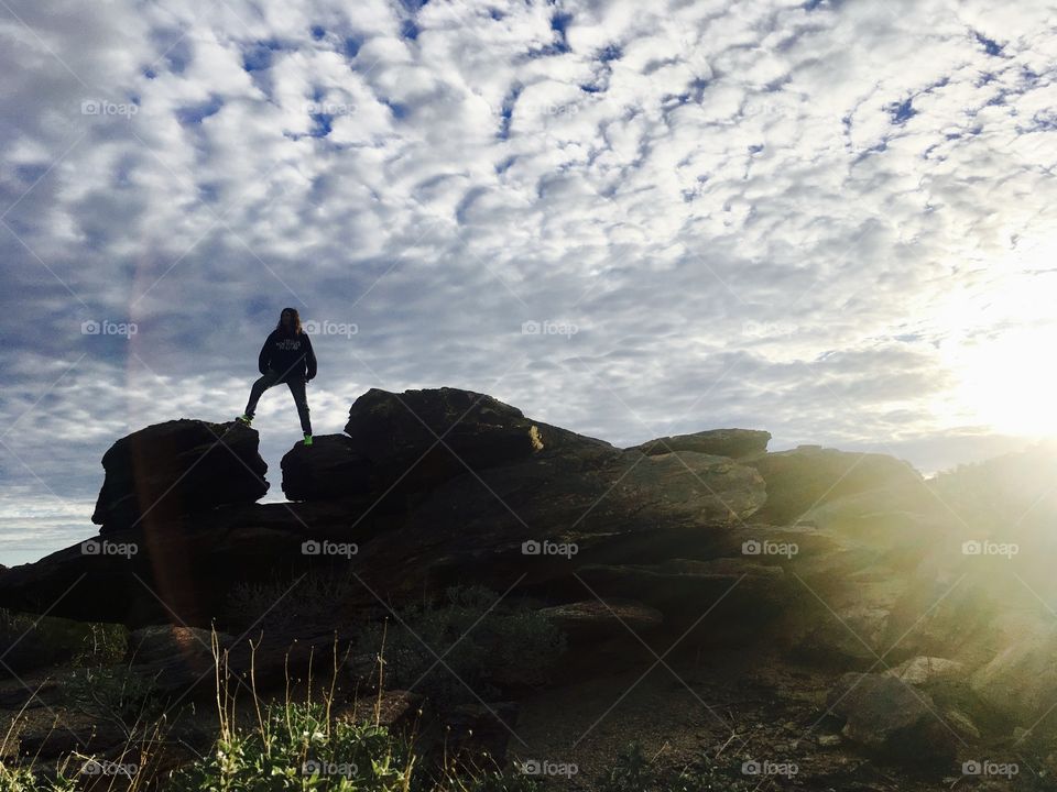 A hiker posing atop some rocks during sunrise on South Mountain in Phoenix, Arizona
