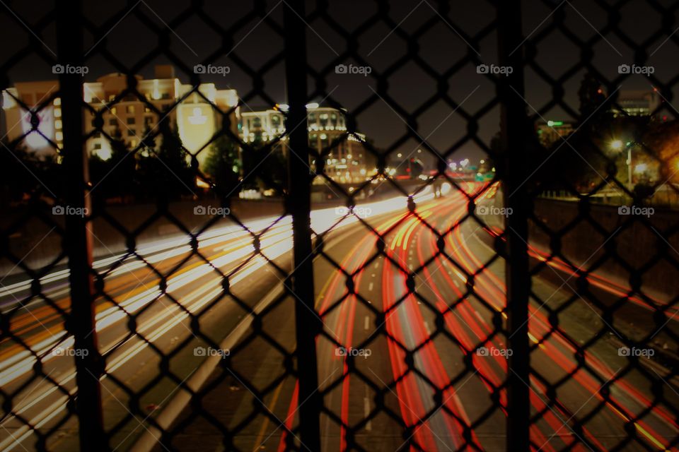artificial car lights on the I-5 freeway. fence. night time. Buildings. cars.