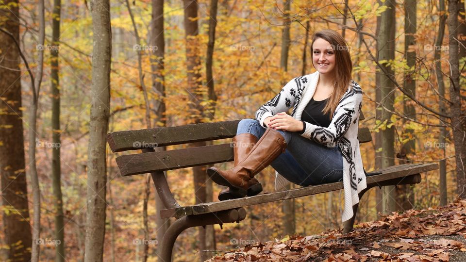 Happy woman sitting on bench near autumn trees