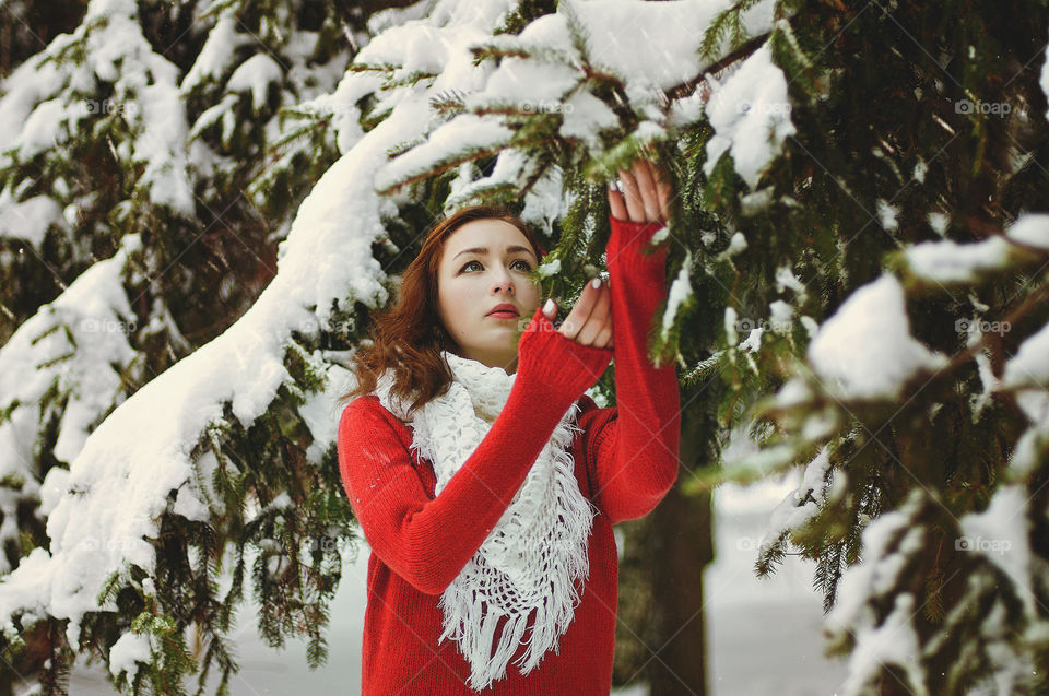 Winter portrait of young redhead woman in red sweater in snowcovered winter park.