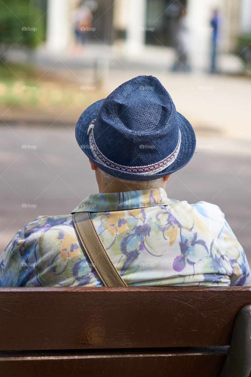 Elderly man with hat sitting in a street bench