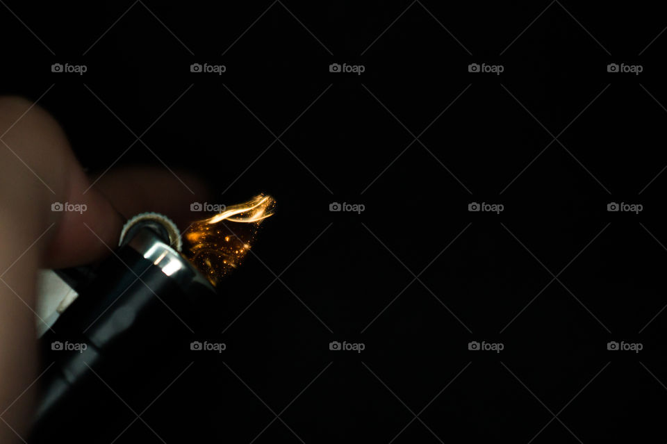 A person has lighters in his hands and he lights it through a flint wheel, the lighter ignites, sparks and fire appear, close-up on a black background.