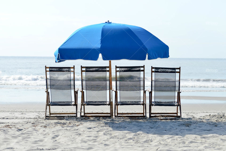 Lounge chairs lined up with an umbrella on the beach overlooking the ocean