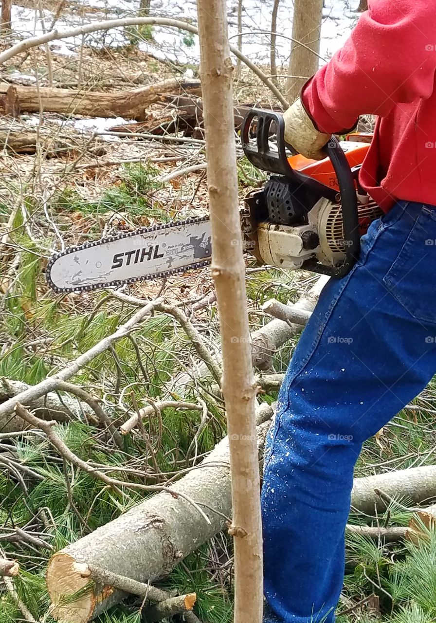 Stihl gas chainsaw, older but still works great & kept in great working condition. Photo shows wood cutter in woods using the Stihl chainsaw, wearing protective work gloves.