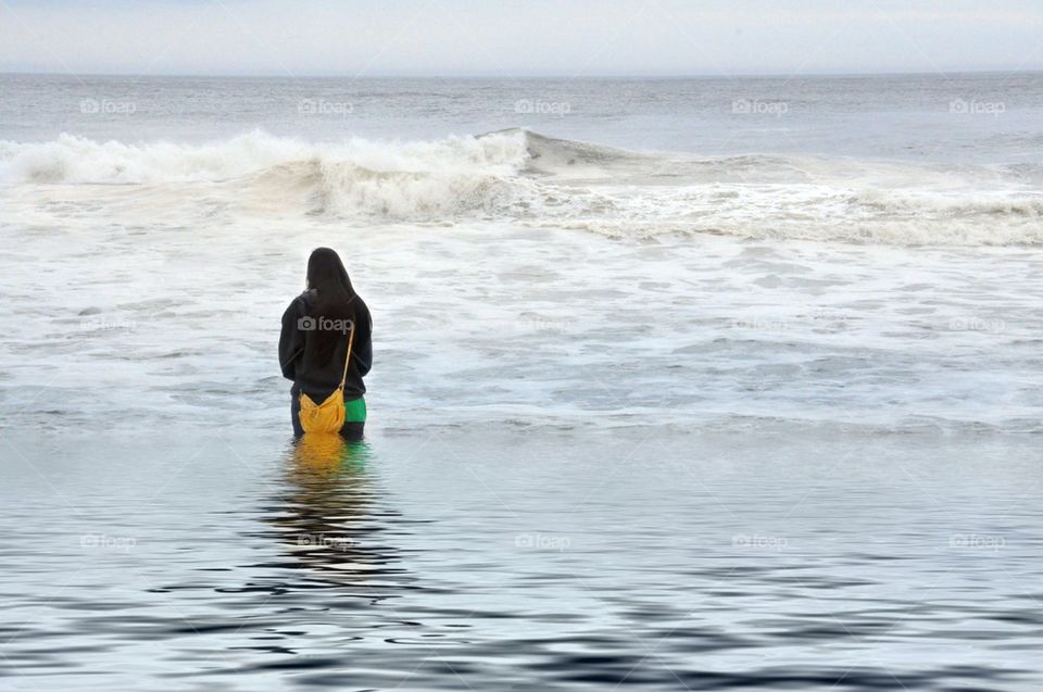 Young girl fully clothed walking into ocean