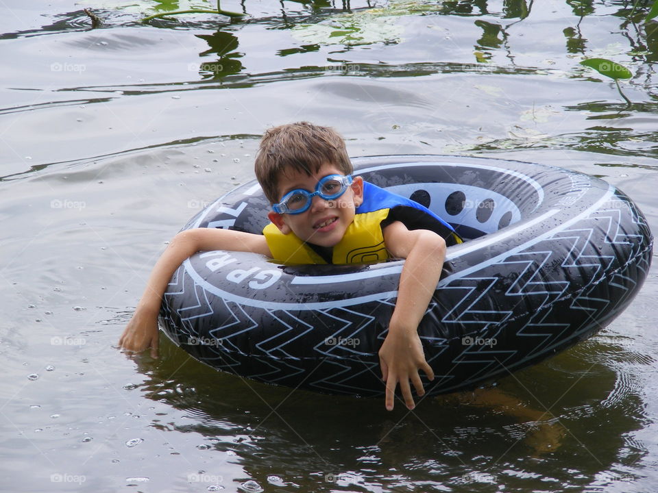 Boy floating on an inner tube in a lake and wearing goggles.