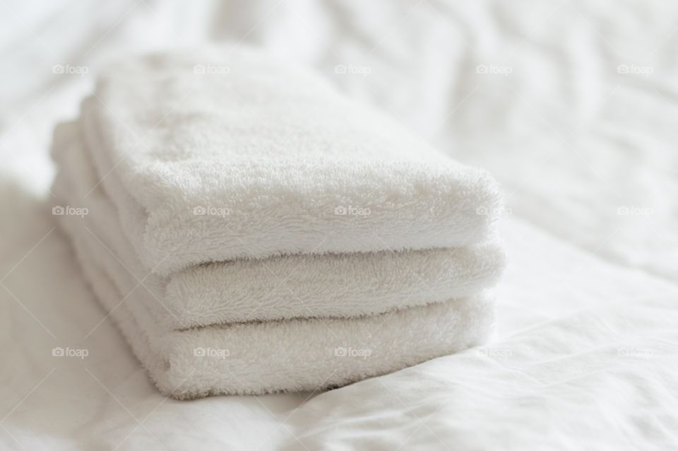 Freshly washed white towels. Freshly washed white hand towels stacked on a white bed.