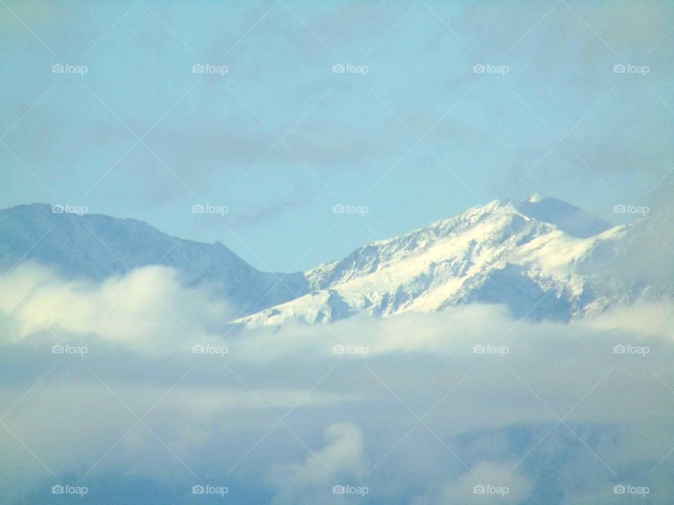 Snow covered mountaintop dooming over the clouds. 