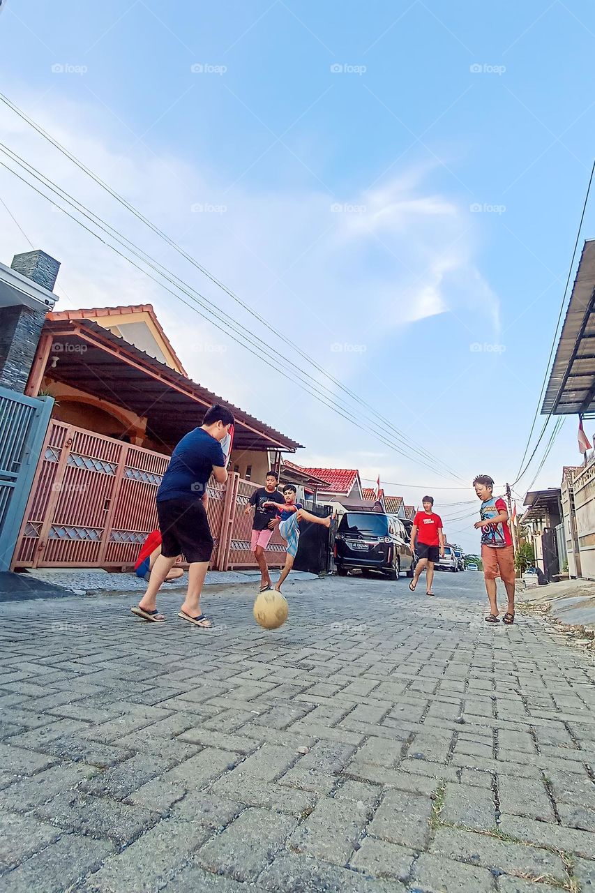 Bandar Lampung, Lampung, Indonesia - December 15, 2023: people playing ball on the rocky road in front of the house