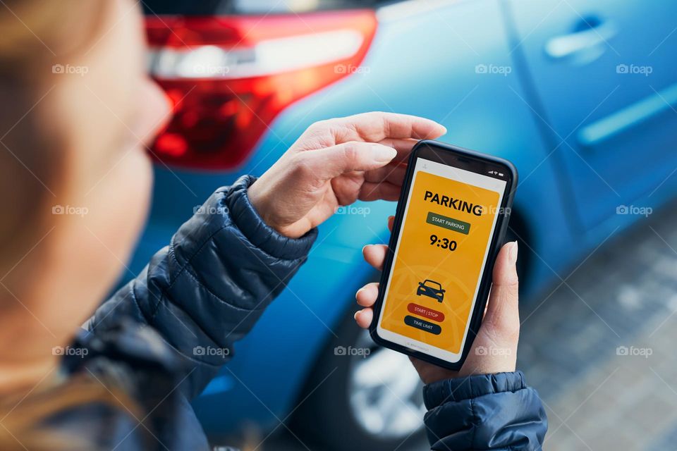 Woman using mobile parking app on smartphone. Driver using smartphone to pay for parking. Car park application on mobile phone. Convienience paying for parking using fast payment online. Mobile park service