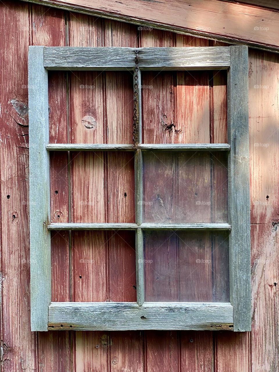 A window frame missing several panes of glass on the side of a wooden structure 