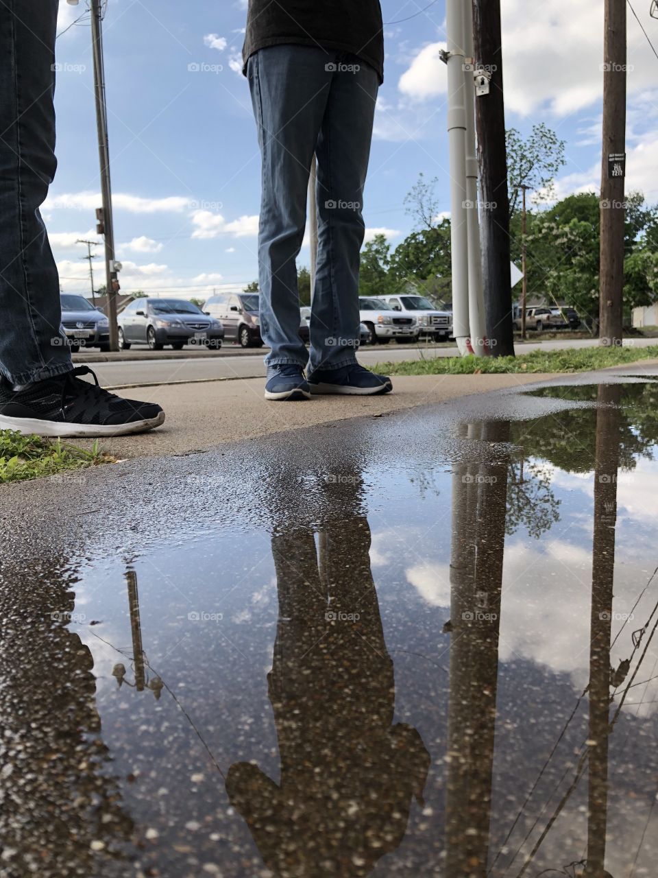 Feet reflected in puddle with parked cars in background