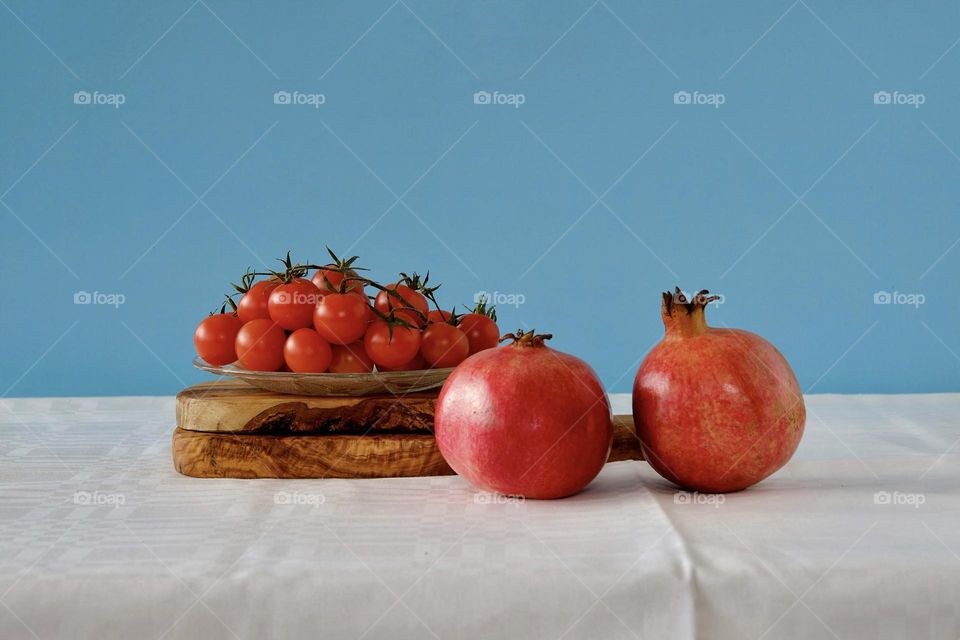 Still life with pomegranate fruits and tomatoes on plate against blue background. 
