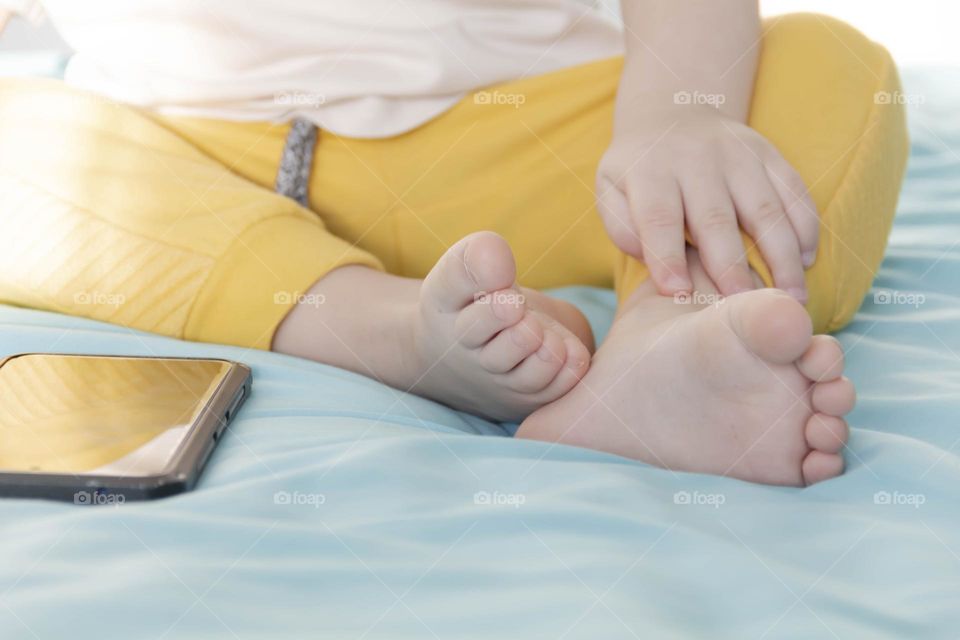 Small feet of a toddler in business pants on the bed with a mobile phone nearby.