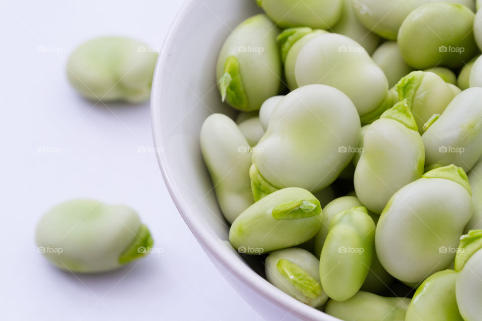 A bowl full of fresh broad beans on a white background.