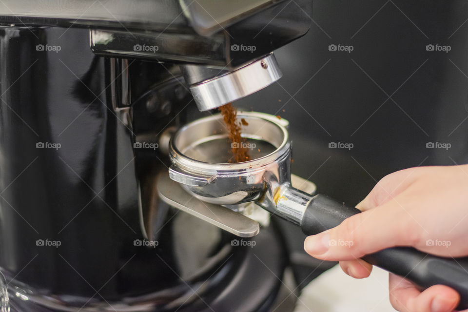 Close-up shot of freshly ground coffee in a grinder in a cafe by a barista man is using a tamper to press freshly ground morning coffee into a coffee tablet in a cafe by a barista