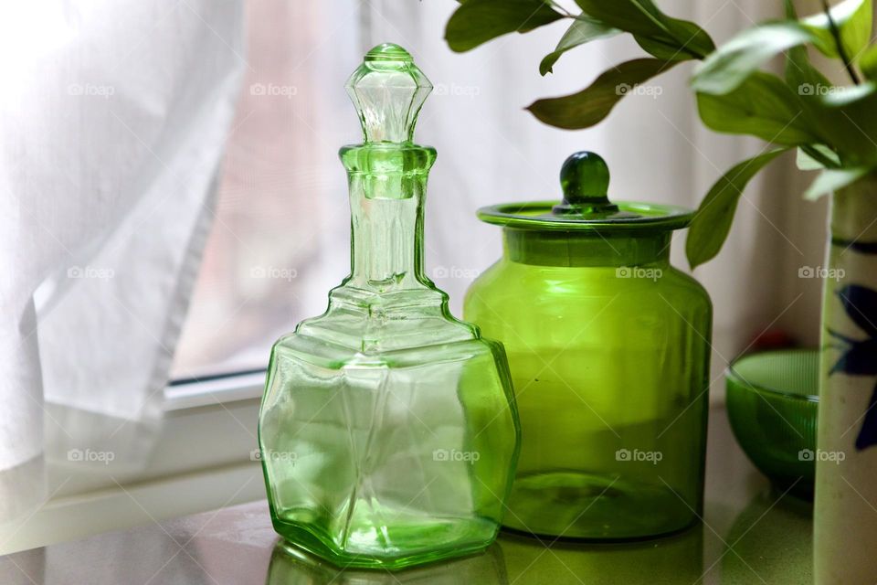 Green glass decanter and jar on countertop illuminated in natural light in front of white curtained window, vintage, antique and collectible. Room for text. Home decor, collecting, food and beverage storage