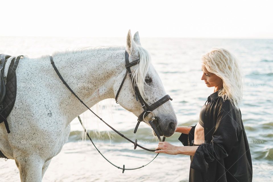 Young long hair woman in black shirt with white horse on seascape background