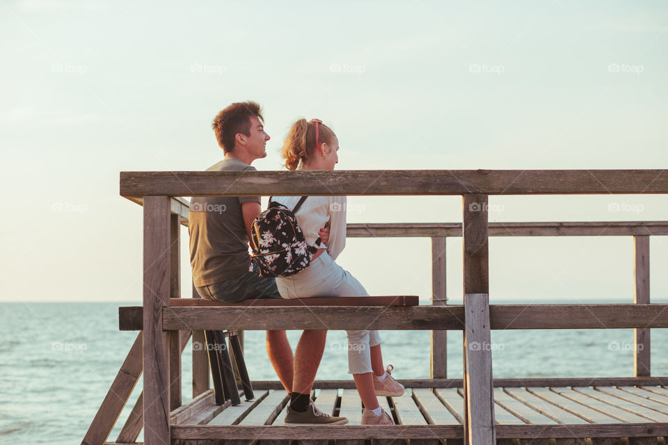 Happy smiling couple of young woman and man sitting on a pier over the sea during summer vacations. Copy space room for text