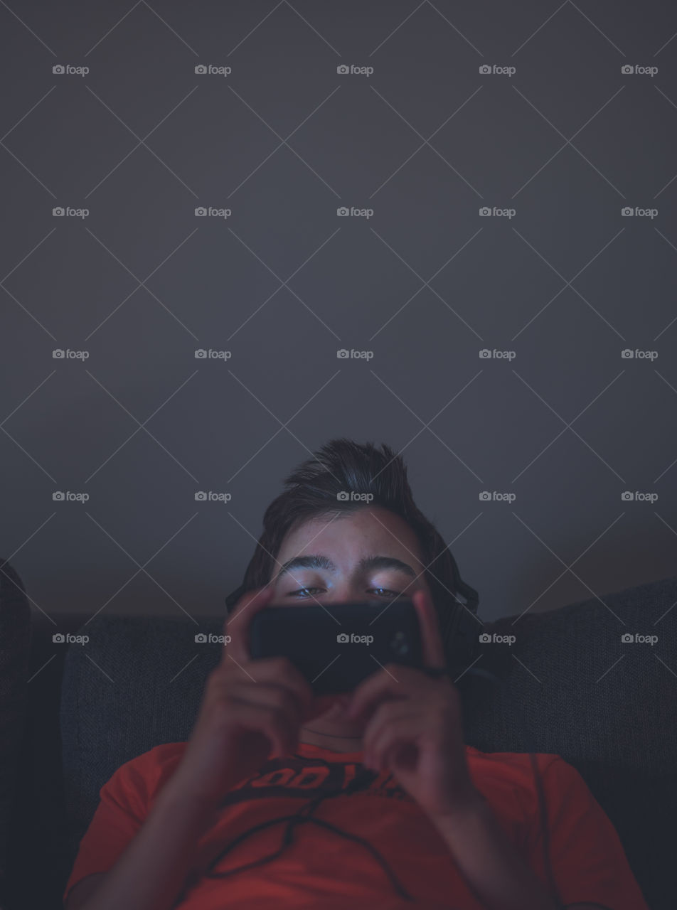 Illuminated by light. Illuminated by glowing light of screen. Boy looking at mobile phone screen.