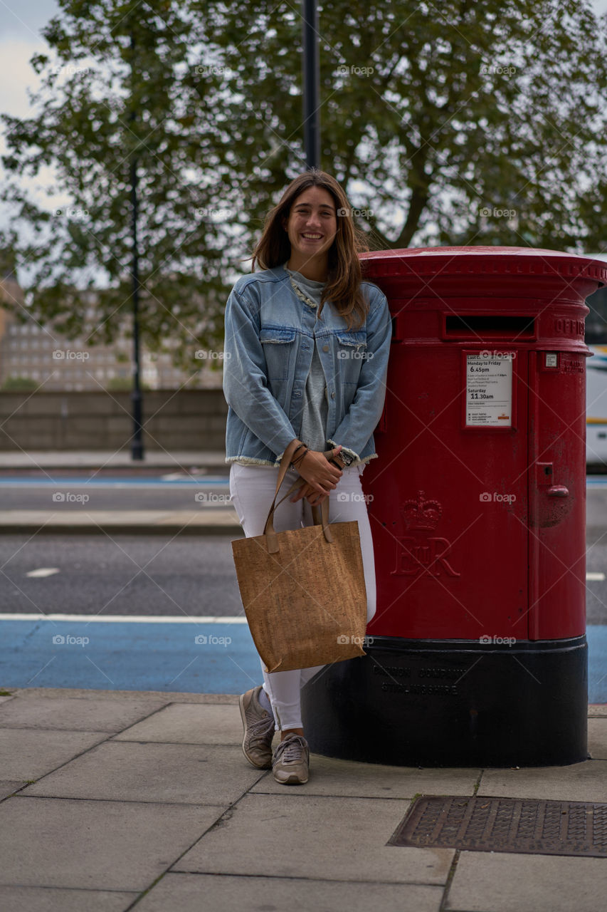 Happy young woman leaning on red letterbox