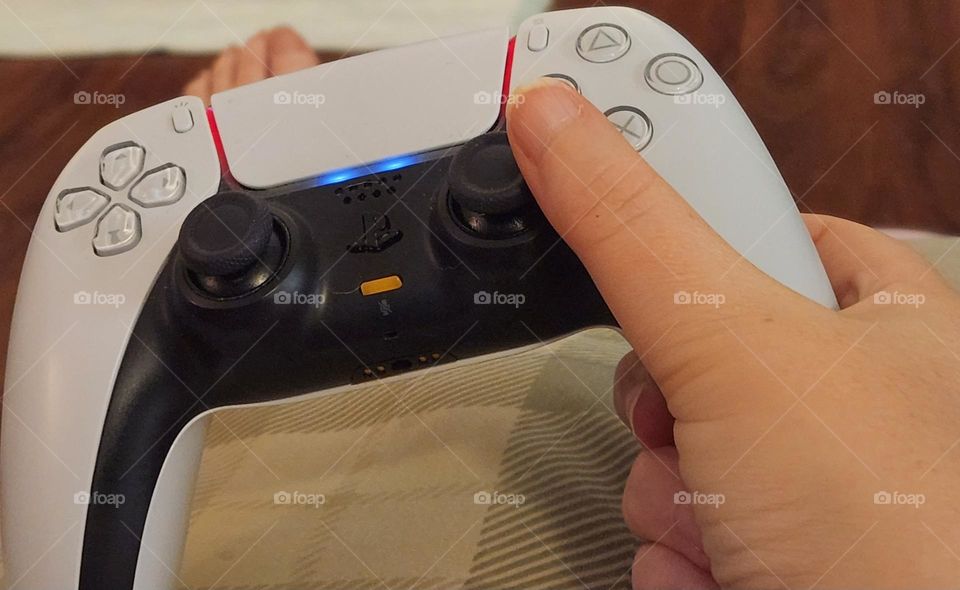 close up view of a woman's hand using a black and white Playstation controller with blue light to play a video game